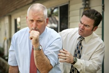 A mature businessman with a severe cough.  His worried colleague is patting him on the back.  Focus on coughing man.  