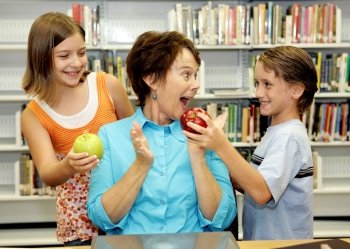 Two students giving apples to their favorite teacher.  She is very surprised and happy.