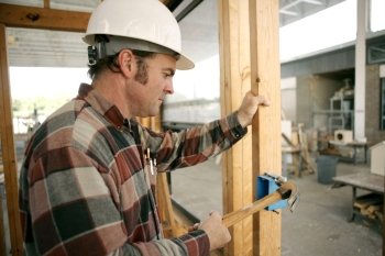 An electrician on a construction site hammering a switch box into a wood beam.  Model is a licensed master electrician. Work being performed to code.