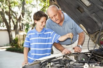 Father and son working on the car together.  The son is checking the oil.  