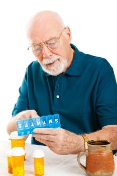 Senior man uses a pill organizer to prepare his medication for the week.  White background.