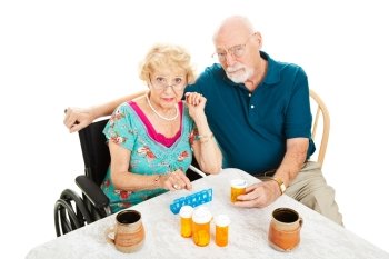 Senior couple frustrated by health issues, sitting at the table surrounded by pill bottles.  Isolated on white.  