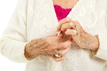 Senior woman’s arthritic hands struggling to button her sweater.  