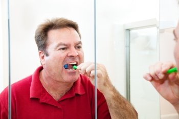 Man in his forties brushes his teeth looking in the bathroom mirror.  