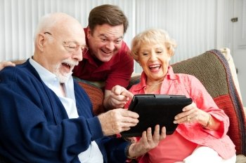 Laughing family, senior parents and their adult son, using a tablet PC.  