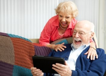Senior couple laughing while using their tablet pc to video chat with their grandkids.  