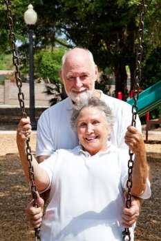 Romantic senior husband pushing his lovely wife in a swing on a playground.  