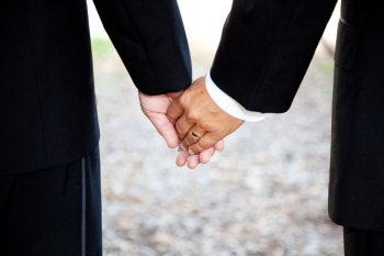 Closeup of a gay couple holding hands, wearing a wedding ring.  Couple is a hispanic man and a caucasian man.