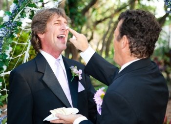 One groom playfully puts wedding cake on his husband’s nose at their wedding.