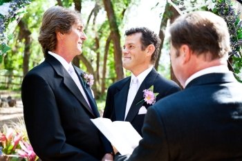 Gay male couple saying their marriage vows before a minister in lovely outdoor setting.  