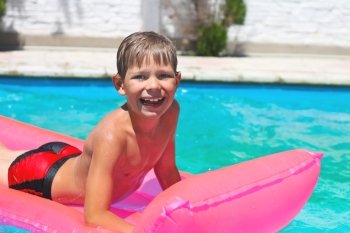 Smiling boy lies on pink mattress in the pool 