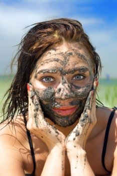 Pretty young woman having mud bath outdoors
