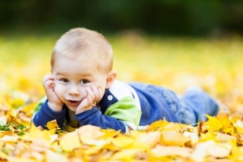 little boy lying on the yellow leaves in the autumn park