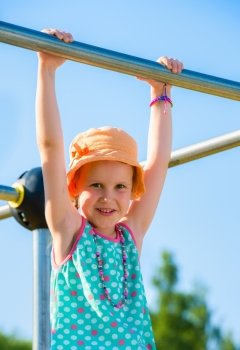 Young girl hangs on the jungle gym, sunny day