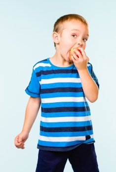 Little boy on striped t-shirt eating apple, studio shot and light blue background