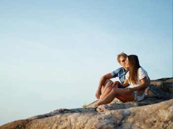 Young couple sits together on the cliff, blue sky on background
