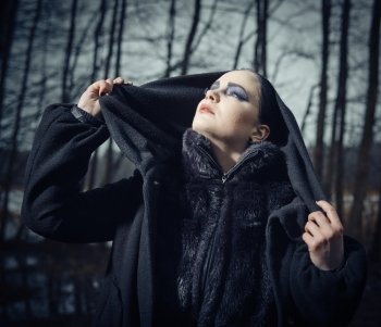 Fashion woman wearing a winter coat and she pose in a gloomy forest, cold rainy weather, cross processed image, close-up