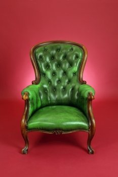 Photo of an old antique green leather chair sitting on a red background.