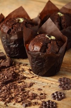 Photo of three moist chocolate muffins resting on an old wood table. Shallow depth of field focusing on front muffin.