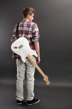 Photo of a teenage male standing with a white electric guitar slung over his back.
