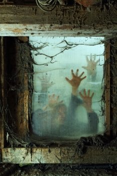 Photo of zombies outside a window that is covered with spiderwebs and filth.
