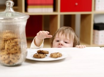 Photo of a nineteen-month-old stealing cookies from a plate on a table with a full cookie jar beside.