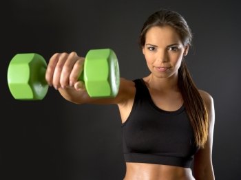 Photo of a beautiful female doing a front shoulder fly with a dumbbell over a dark background.