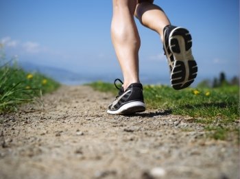 Photo of the legs and shoes of a young woman jogging on a gravel path down a country path. Slight motion blur visible.