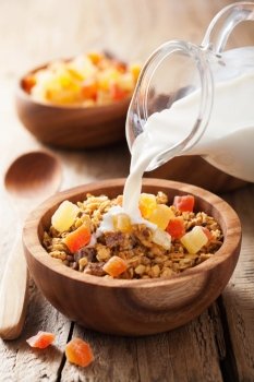 pouring milk over healthy granola with dry fruits for breakfast