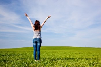 Young beautiful woman with hands up on green sunny field