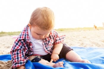 Handsome curious child sitting on sand on the beach playing, sunny day.