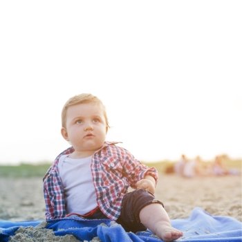 Handsome curious child sitting on sand on the beach looking at the sky at sunny day.