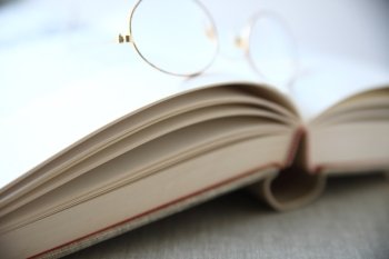 A pair of reading glasses rests on an open book.