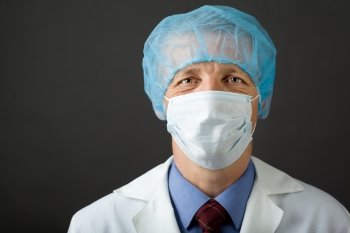 Male physician in mask and cap looking at camera