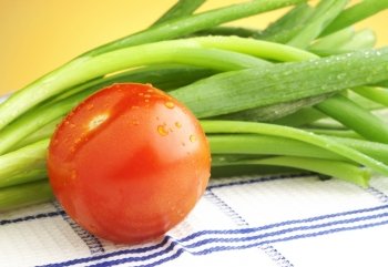 Red ripe fresh tomato with leafy green spring onions on yellow background.