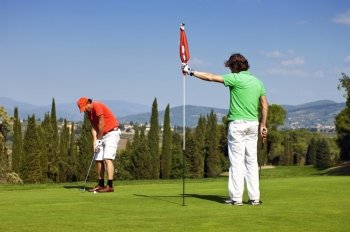 Flight of two golfers playing on the green of a golf course