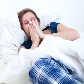 A girl blowing her nose while lying sick in bed.