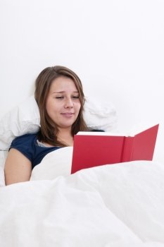 Young woman reading an entertaining book in bed