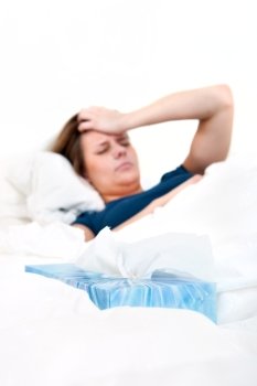 Tissue box in between the sheets, with a young woman, suffering from a severe headache, lying in bed, sick