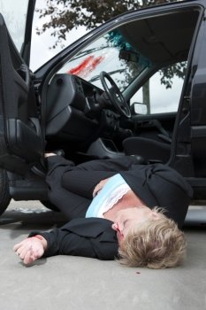 An injured driver with a severe head wound, lies unconsciously on the ground, fallen from her vehicle after an accident