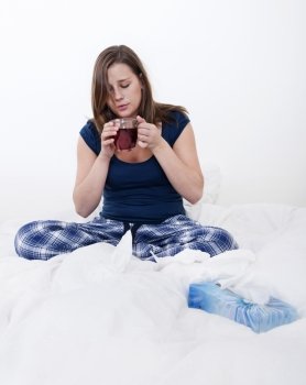 Young woman drinking a cup of tea in bed, whilst being home sick with flu