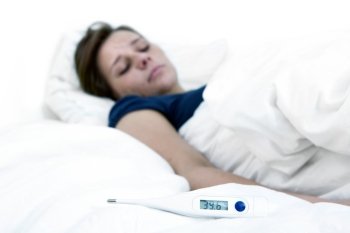 Thermometer, indicating high fever, lying on a bed, with a sick woman in the background