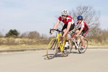 Active male cyclists in sportswear riding cycles on an open country road