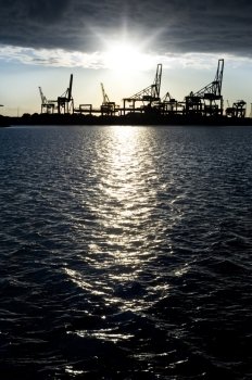 Silhouette of an industrial harbour against a bright sunset, reflected in the dark, cold water 