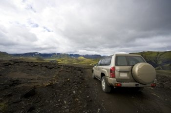 An all terrain car emerging from the grim lava fields into the meadows of the beautiful Landmannalaugar national park in Iceland