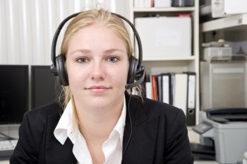 A woman wearing a head set with microphone as receptionist for a small business. An office setting in the background