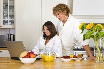 Young couple wearing bath robes enjoying a healthy breakfast in a kitchen behind a laptop