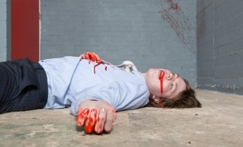 Murder victim lying on the floor, being shot in a basement, with blood splatter on the wall