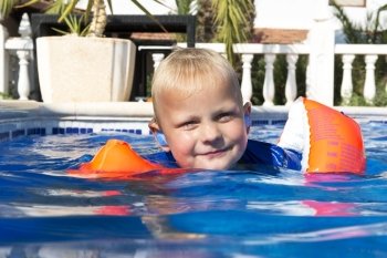 Young boy wearing inflatible floating wings learning to swim in an outdoor pool