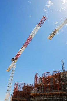 Construction cranes and scaffolding building under construction against blue sky